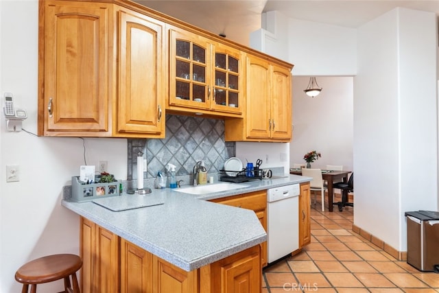 kitchen with tasteful backsplash, light countertops, glass insert cabinets, a sink, and dishwasher