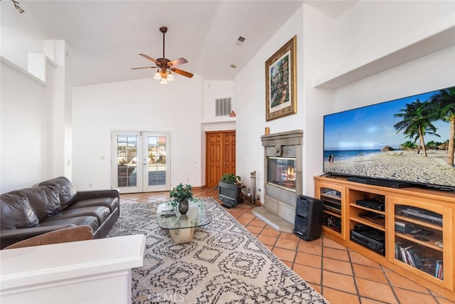 living area featuring french doors, visible vents, a glass covered fireplace, light tile patterned flooring, and high vaulted ceiling