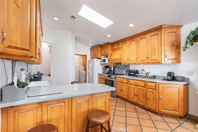 kitchen with white appliances, a peninsula, light countertops, a kitchen bar, and a sink