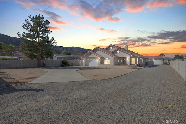 mediterranean / spanish house with an attached garage, a mountain view, fence, concrete driveway, and a chimney