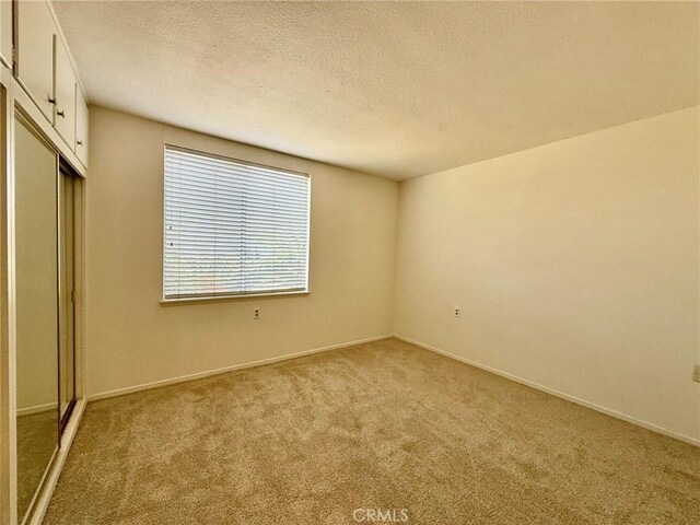 unfurnished bedroom with light colored carpet, a textured ceiling, and a closet