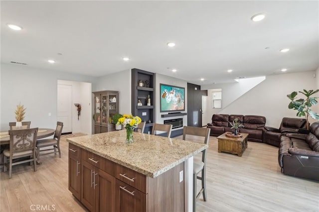 kitchen with a center island, a kitchen breakfast bar, a fireplace, light stone countertops, and light hardwood / wood-style floors