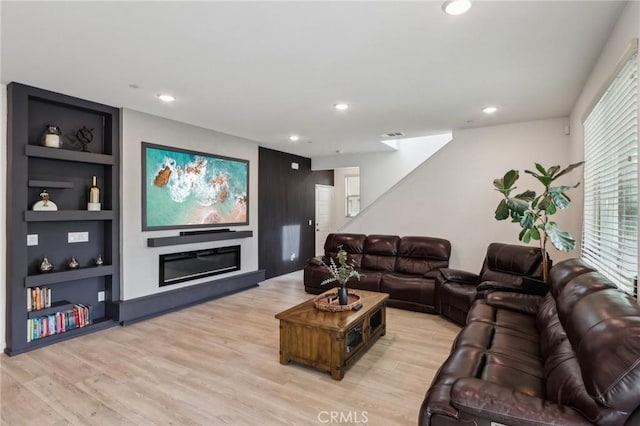 living room with built in shelves and light hardwood / wood-style flooring