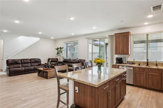 kitchen featuring sink, light hardwood / wood-style flooring, a breakfast bar, a center island, and stainless steel dishwasher