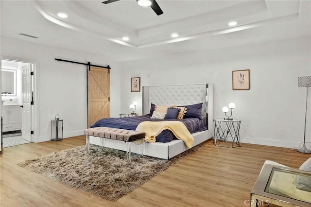 bedroom featuring a barn door, connected bathroom, a tray ceiling, and light hardwood / wood-style floors