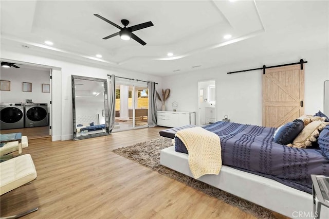 bedroom featuring wood-type flooring, access to outside, independent washer and dryer, a tray ceiling, and a barn door