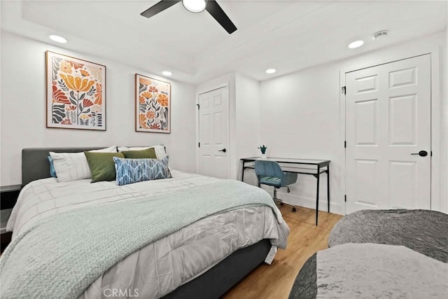 bedroom with a tray ceiling, light hardwood / wood-style floors, and ceiling fan