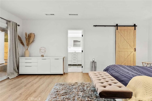 bedroom with ensuite bathroom, a barn door, and light wood-type flooring