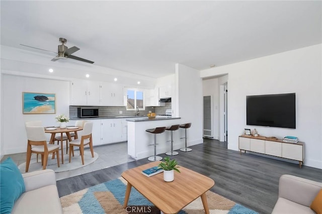 living room featuring ceiling fan, sink, and dark hardwood / wood-style floors