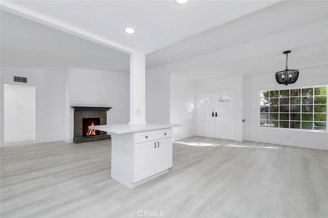 kitchen featuring decorative light fixtures, a kitchen island, white cabinetry, and light hardwood / wood-style floors