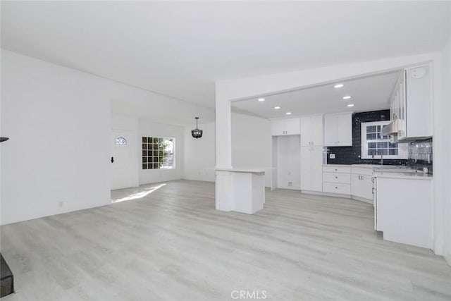 kitchen with white cabinetry, tasteful backsplash, light wood-type flooring, pendant lighting, and sink