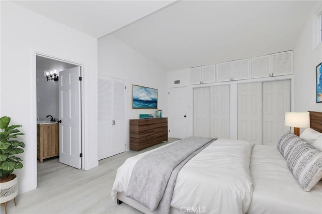 bedroom with light hardwood / wood-style floors, ensuite bathroom, lofted ceiling, and multiple closets