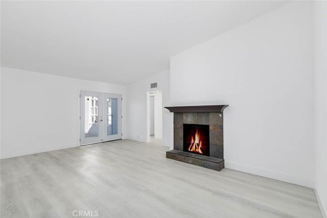 unfurnished living room featuring light hardwood / wood-style floors, a tile fireplace, french doors, and vaulted ceiling