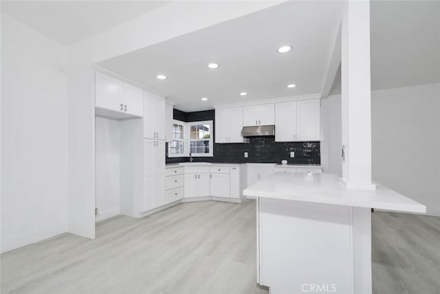 kitchen with white cabinetry, sink, kitchen peninsula, light hardwood / wood-style flooring, and a breakfast bar area