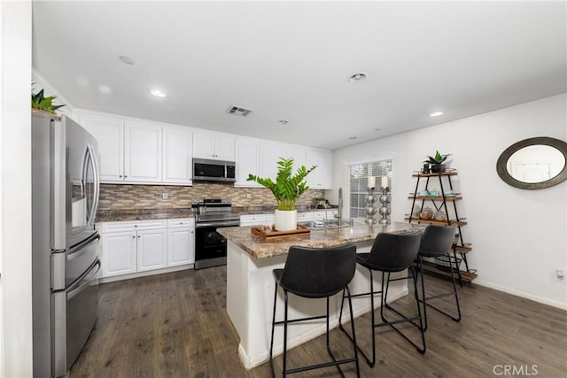 kitchen with stone counters, white cabinets, an island with sink, stainless steel appliances, and a breakfast bar area