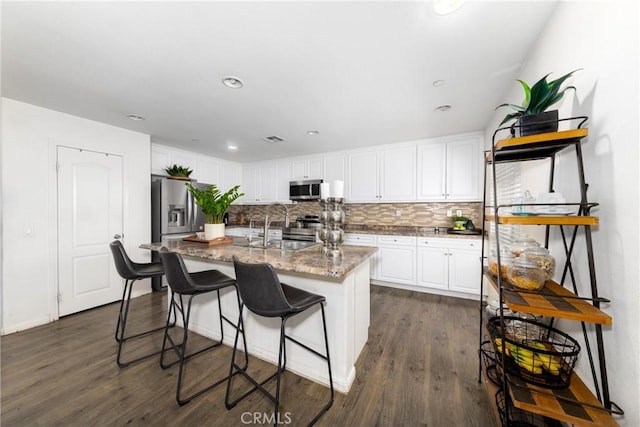 kitchen featuring white cabinets, stainless steel appliances, dark stone countertops, sink, and a center island with sink