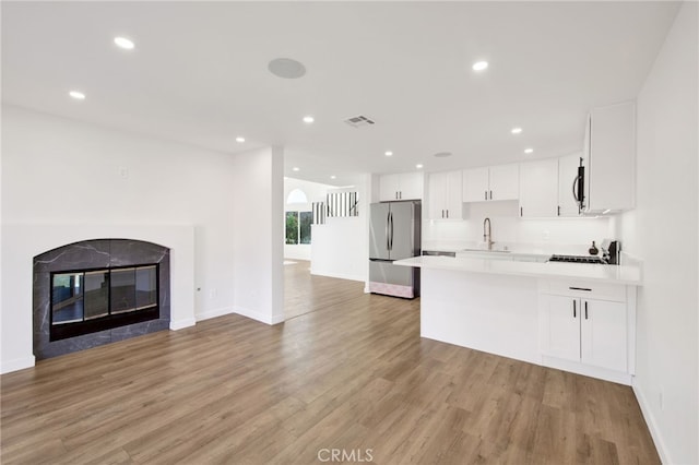 kitchen with white cabinetry, light hardwood / wood-style floors, stainless steel appliances, a tiled fireplace, and sink