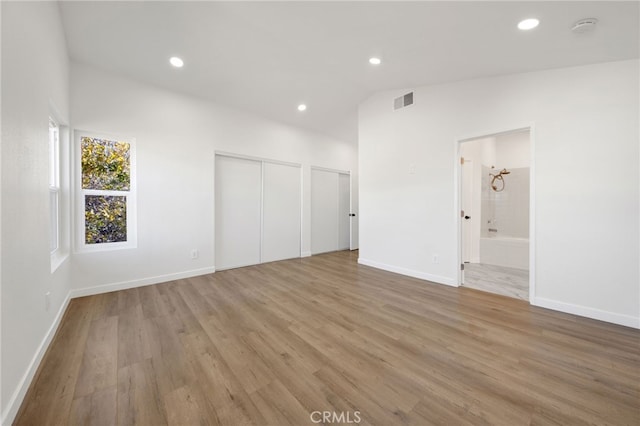 unfurnished bedroom featuring connected bathroom, lofted ceiling, and light wood-type flooring