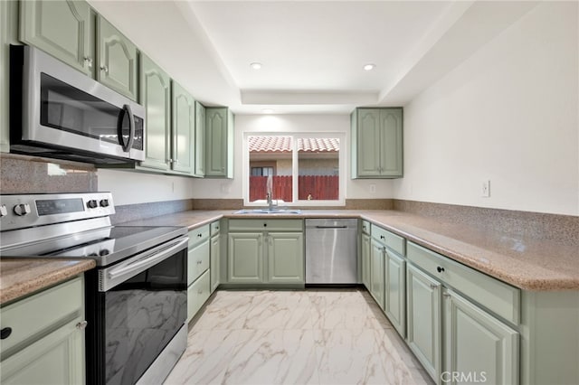 kitchen with a raised ceiling, green cabinetry, sink, and stainless steel appliances