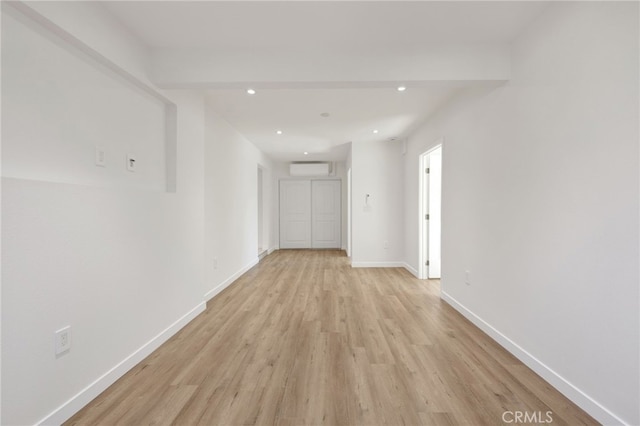 corridor with an AC wall unit and light wood-type flooring