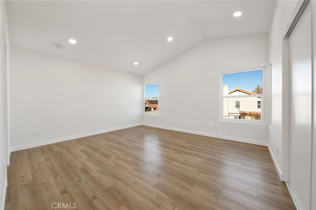 spare room with light wood-type flooring and lofted ceiling