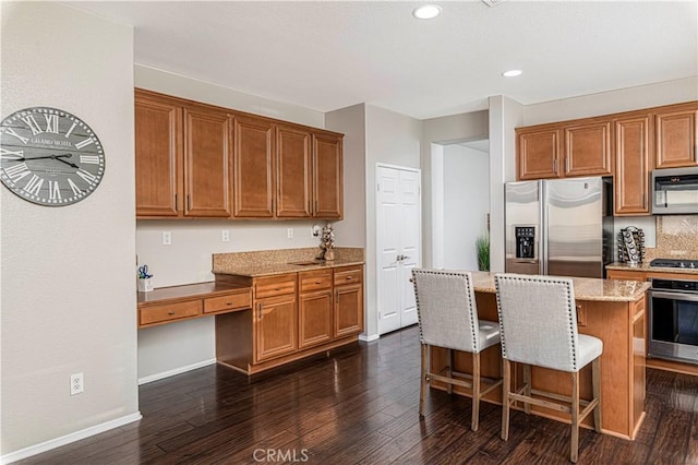 kitchen featuring stainless steel appliances, a center island, built in desk, light stone countertops, and dark hardwood / wood-style flooring