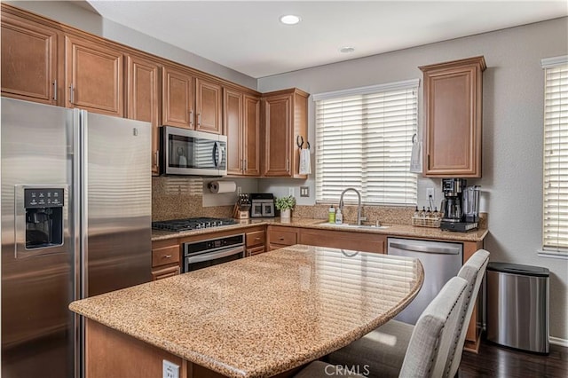 kitchen featuring appliances with stainless steel finishes, a wealth of natural light, sink, a center island, and light stone countertops