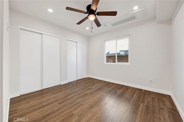 unfurnished bedroom featuring dark wood-type flooring, ceiling fan, and two closets