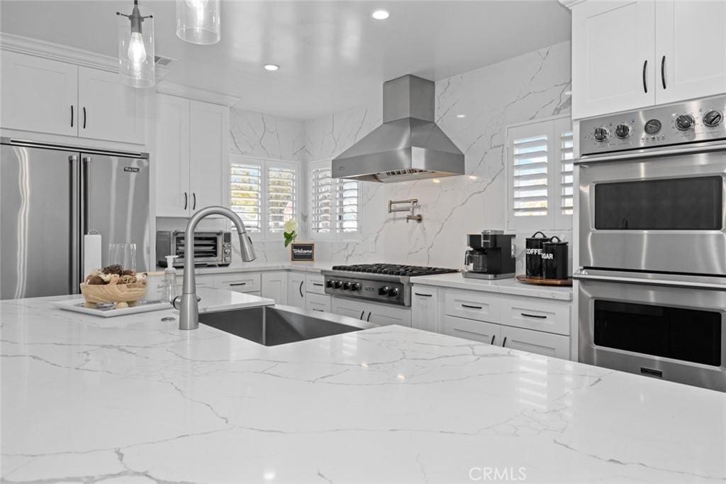 kitchen featuring a toaster, stainless steel appliances, white cabinets, light stone countertops, and exhaust hood