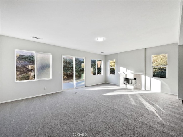 unfurnished living room featuring heating unit, visible vents, a glass covered fireplace, carpet flooring, and baseboards