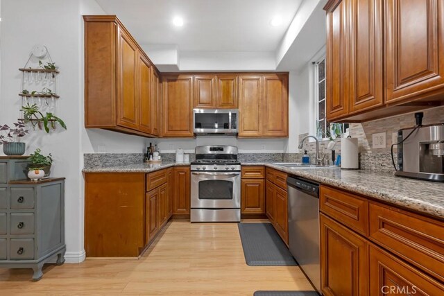 kitchen with light stone counters, stainless steel appliances, light hardwood / wood-style floors, and sink