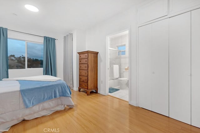 bedroom featuring hardwood / wood-style flooring, connected bathroom, multiple windows, and a closet