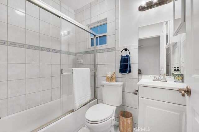 full bathroom with tile walls, vanity, enclosed tub / shower combo, and toilet