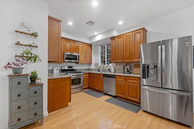 kitchen featuring stainless steel appliances, light stone countertops, sink, and light wood-type flooring