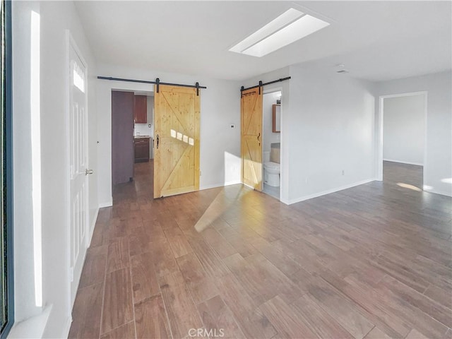 unfurnished room featuring hardwood / wood-style floors, a skylight, and a barn door