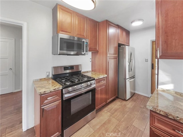 kitchen with light stone countertops, appliances with stainless steel finishes, and light hardwood / wood-style flooring