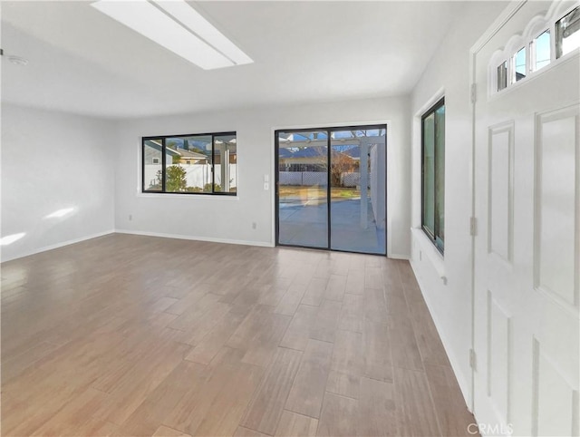 empty room with a skylight and light hardwood / wood-style flooring