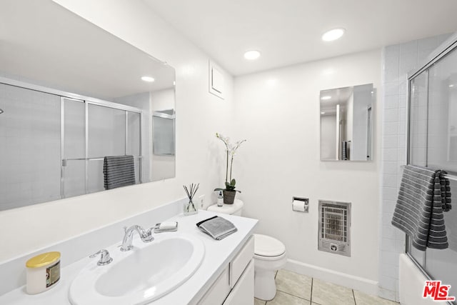 full bathroom featuring toilet, vanity, tile patterned flooring, combined bath / shower with glass door, and heating unit