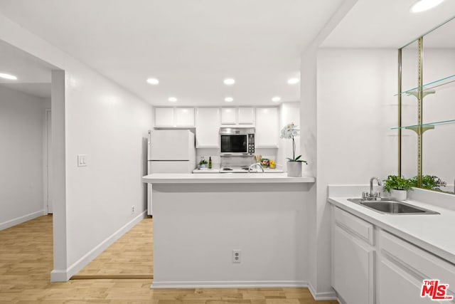 kitchen with kitchen peninsula, sink, white cabinetry, light hardwood / wood-style flooring, and white refrigerator