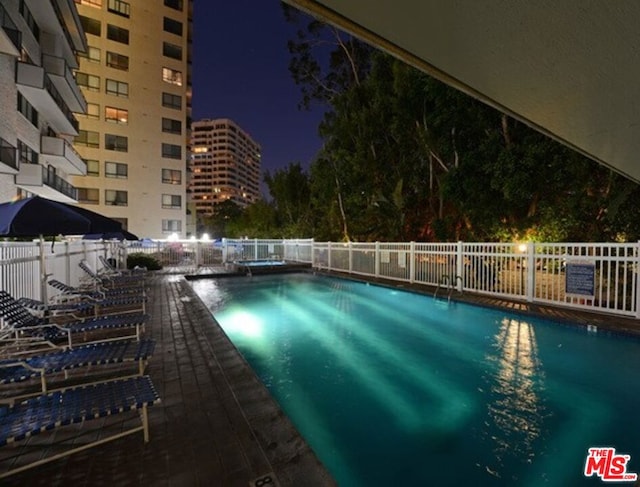 pool at night featuring a patio area