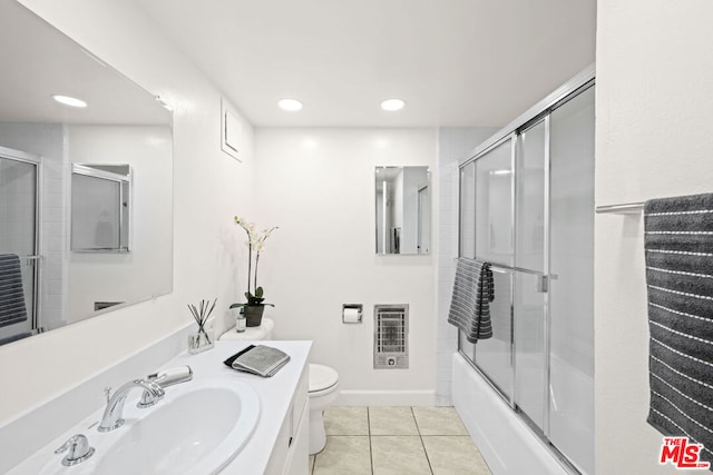 full bathroom with toilet, vanity, tile patterned floors, heating unit, and shower / bath combination with glass door