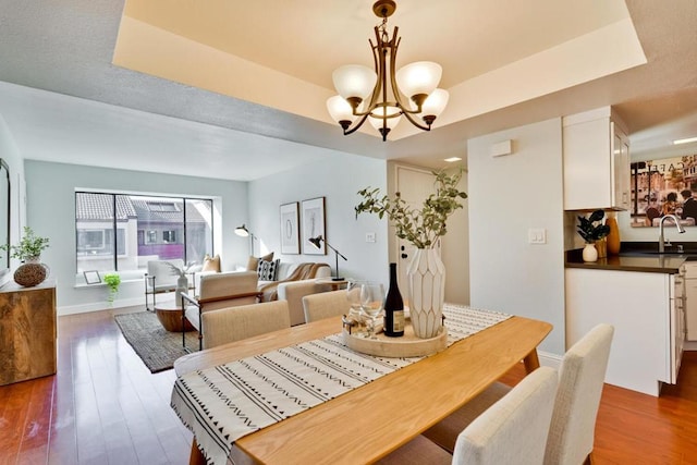 dining space with a notable chandelier, sink, dark wood-type flooring, and a raised ceiling