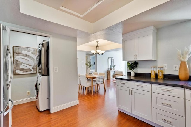 kitchen featuring stacked washer / dryer, white cabinets, light hardwood / wood-style floors, and a tray ceiling