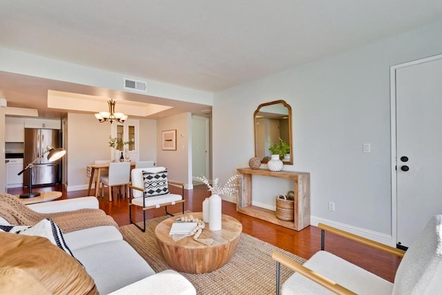 living room with a notable chandelier, hardwood / wood-style flooring, and a raised ceiling