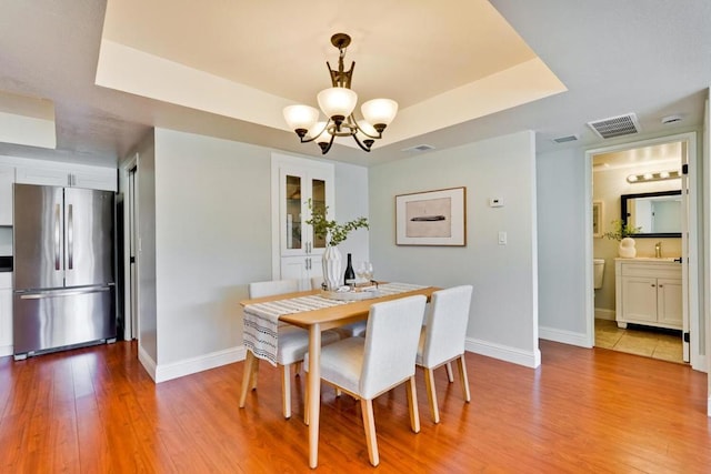 dining space with a tray ceiling, light hardwood / wood-style floors, and a chandelier