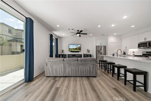 living room with ceiling fan, sink, and light wood-type flooring