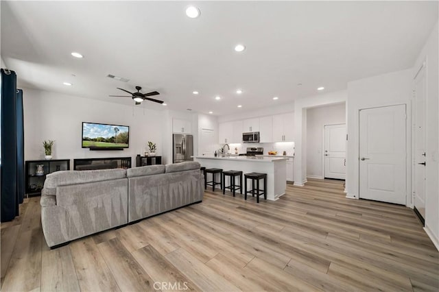 living room featuring ceiling fan, sink, and light hardwood / wood-style floors