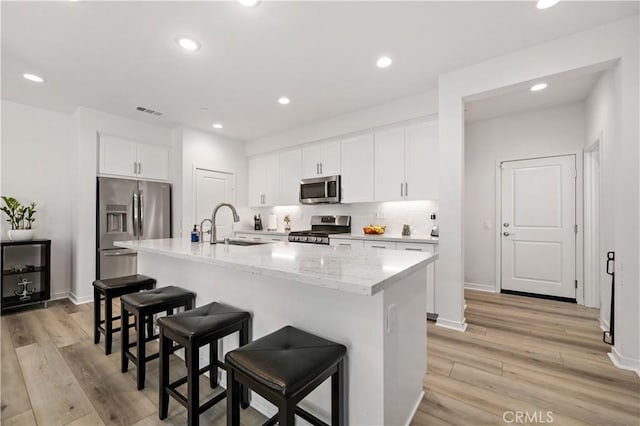 kitchen with white cabinetry, a kitchen breakfast bar, a kitchen island with sink, light stone counters, and stainless steel appliances