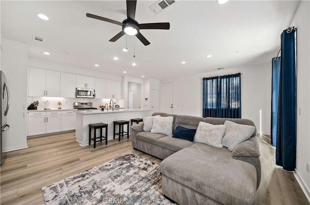 living room featuring ceiling fan, sink, and light wood-type flooring