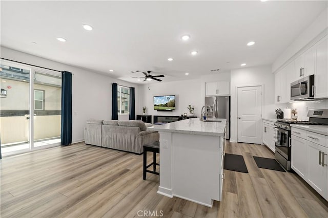 kitchen with appliances with stainless steel finishes, a kitchen island with sink, white cabinetry, a wealth of natural light, and a kitchen bar